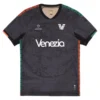 NOCTA Venezia Home Kit 25/26 in black with bold orange and green details, V-neck, short sleeves, front view.